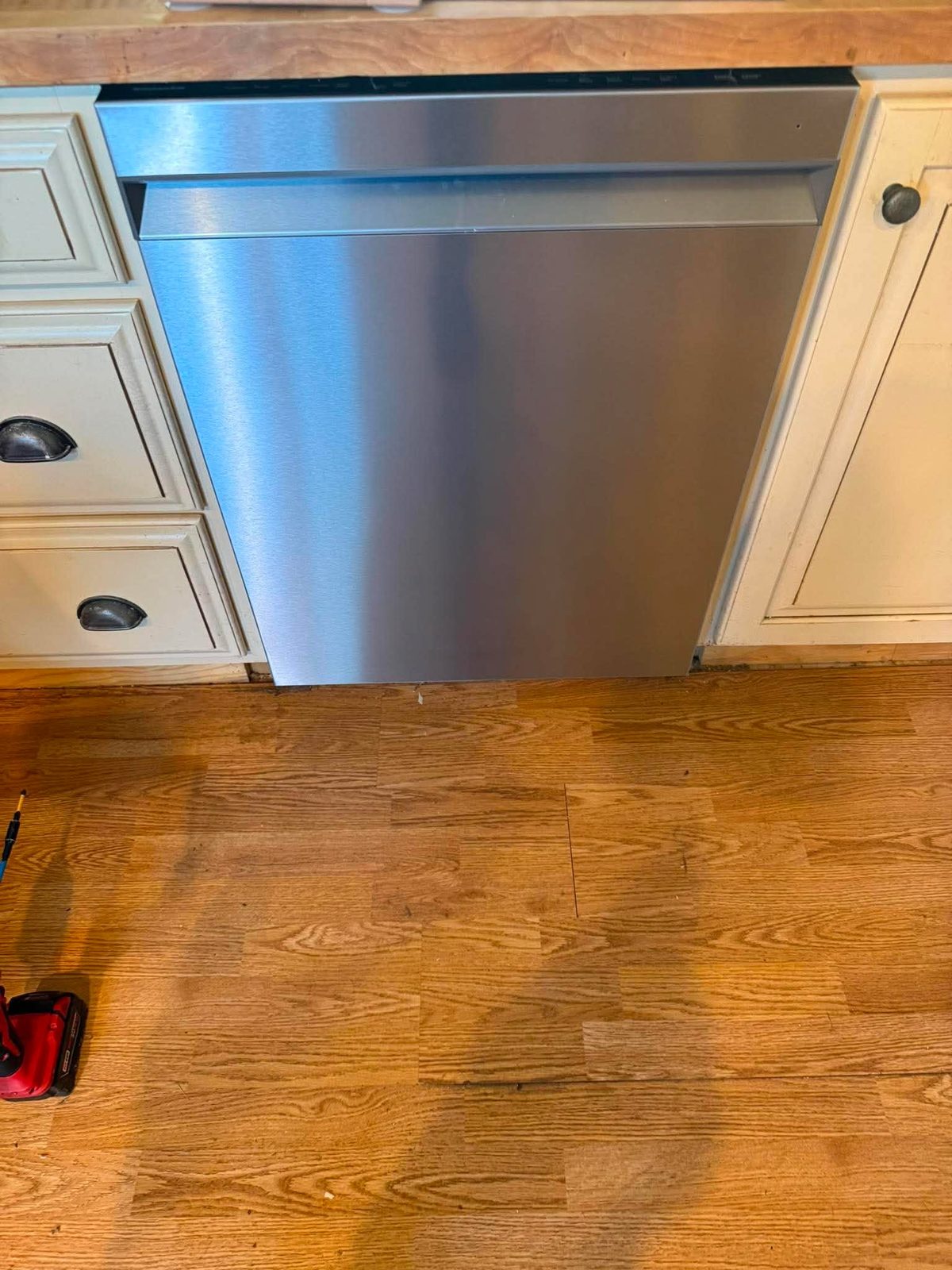 Stainless dishwasher installed under a counter beside oak flooring
