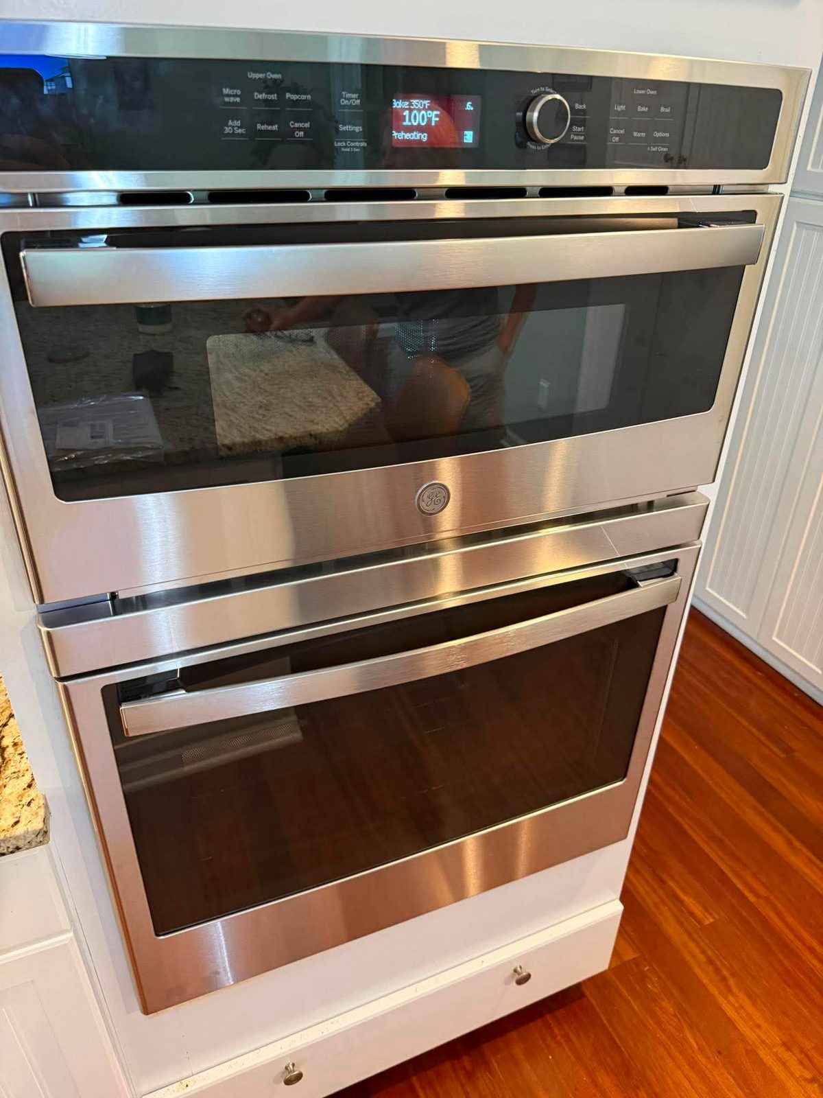Stainless double wall oven installed in white cabinetry, preheating