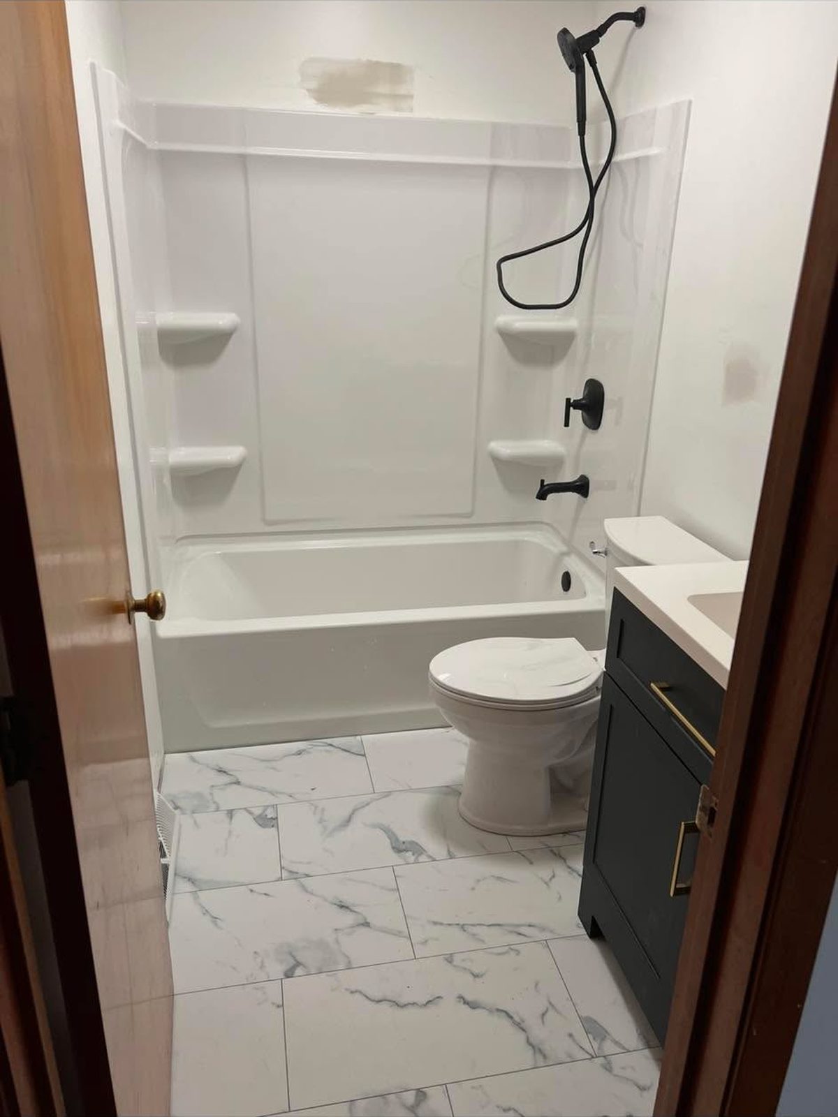 White tub and shower unit with a marble-look tile floor and navy vanity