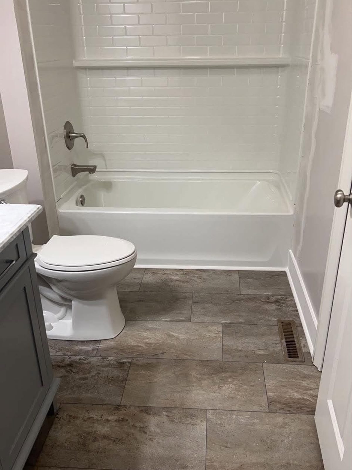 Finished bathroom with a white tub and subway-tile surround over a stone-look tile floor
