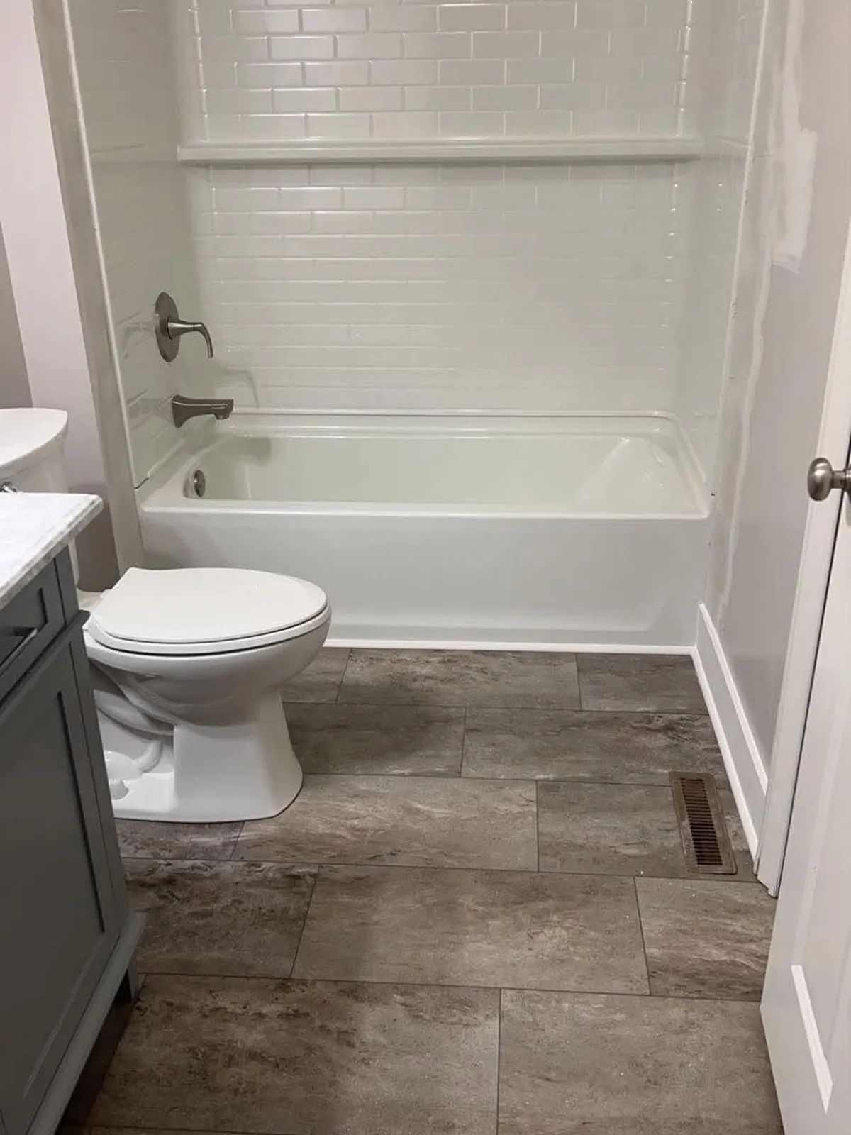 White tub with a white subway-pattern surround over a stone-look floor