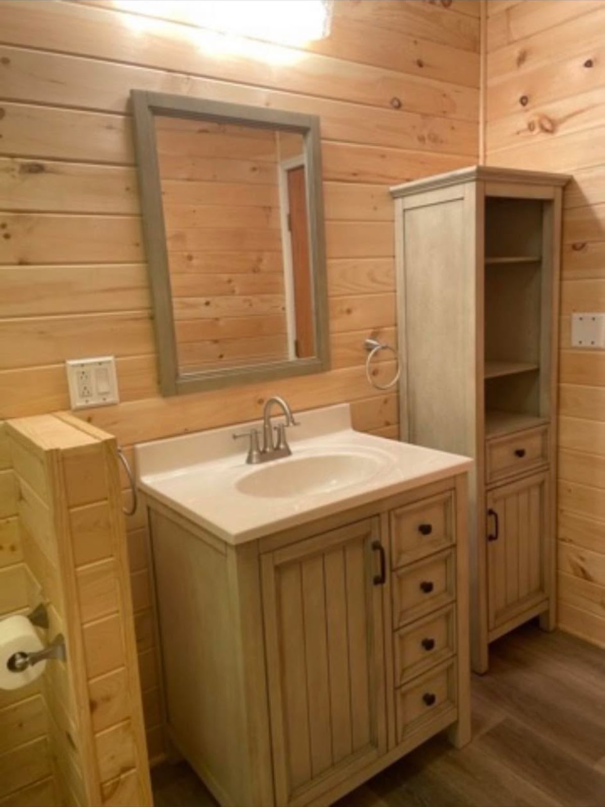 Light wood vanity and matching linen tower against knotty pine walls
