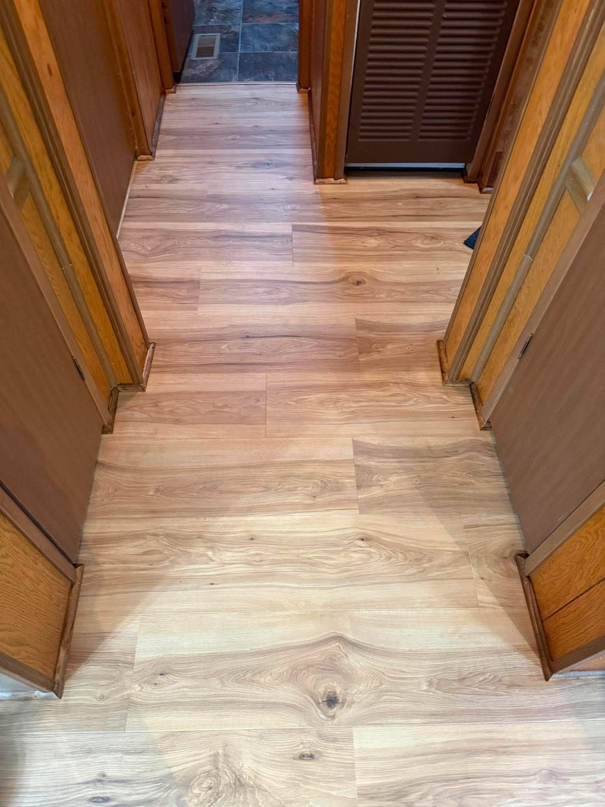 Plank flooring running down a hallway between wood doors