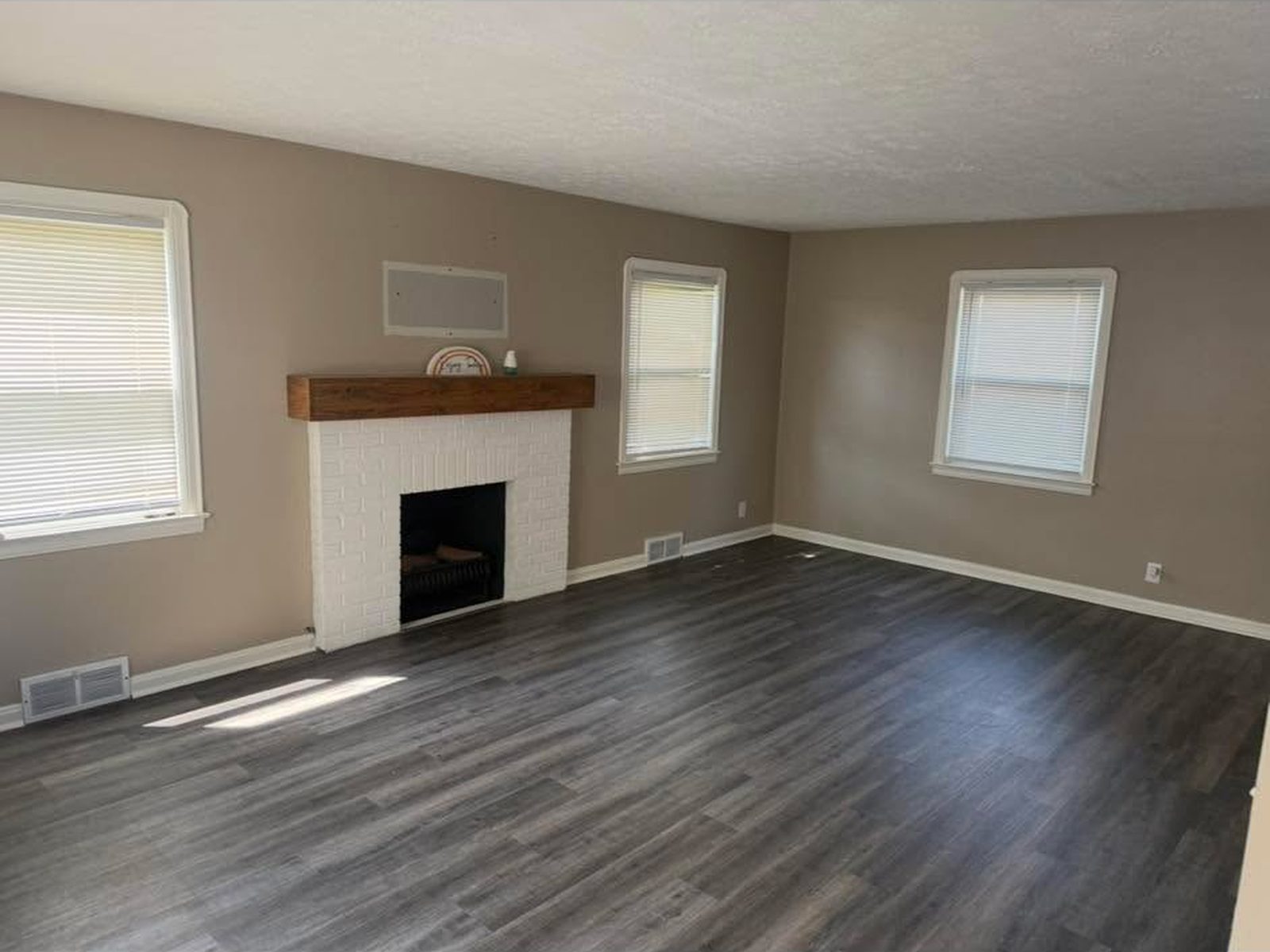 Grey plank flooring across a living room with a white brick fireplace