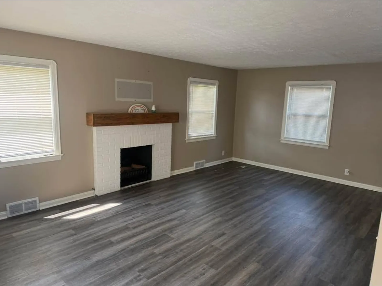 Grey plank flooring across a living room with a white brick fireplace